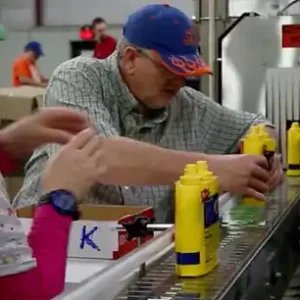 Worker preps mustard bottle for packaging